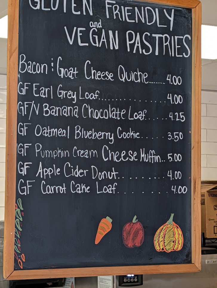 Chalkboard menu of gluten-friendly and vegan pastries, including a gluten-free Earl Grey loaf, apple cider donut, pumpkin cream cheese muffin, and banana chocolate loaf.