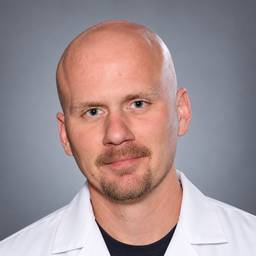 Portrait of Nick Zorn wearing a white lab coat against a gray background