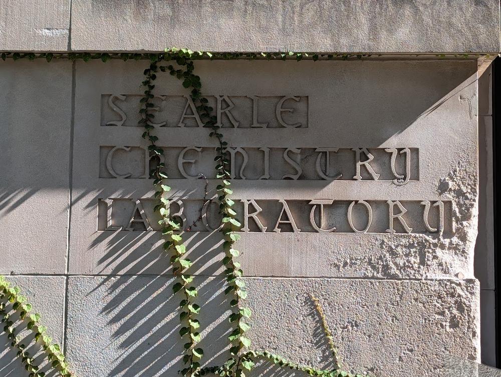 Gothic-style lettering reading Searle Chemistry Laboratory carved into a limestone wall, with ivy hanging across it.